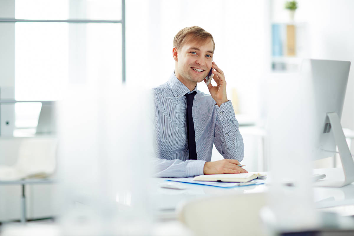 Young businessman speaking on the phone at workplace and looking at camera